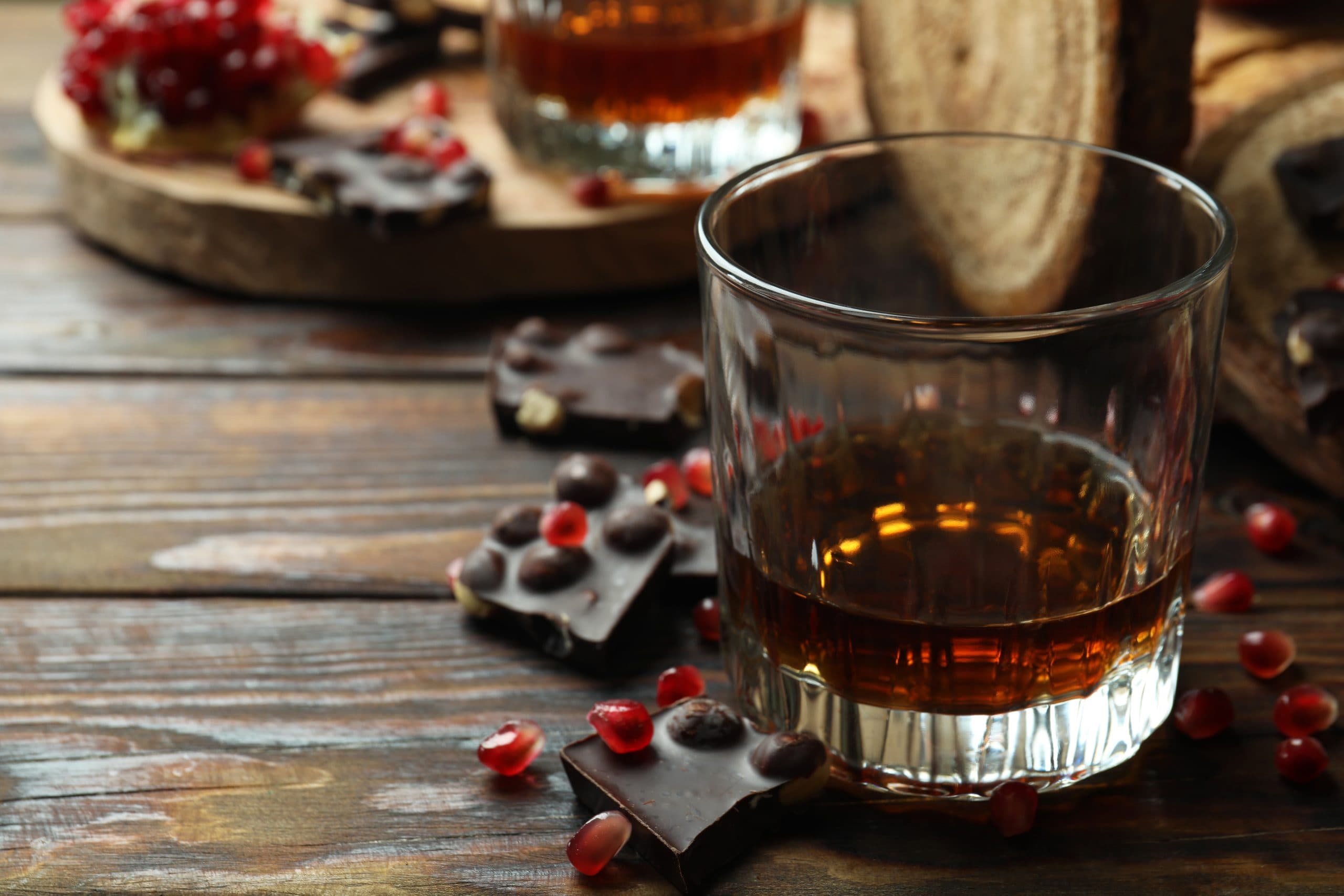 Ett glas rom på ett träbord med chokladbitar och granatäpplekärnor